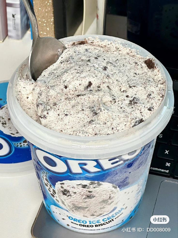 a cup of ice cream with a spoon sticking out of it next to a laptop