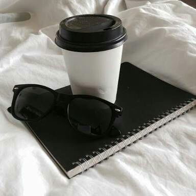 a cup of coffee, sunglasses and notebook on a bed