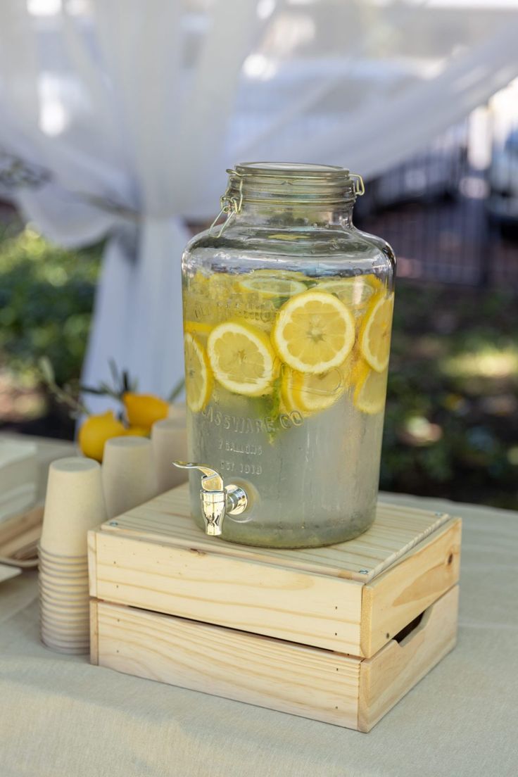 a mason jar filled with lemon slices sitting on top of a wooden box next to cups