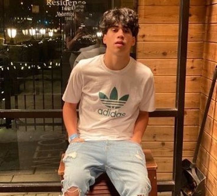 a young man sitting on top of a wooden bench wearing ripped jeans and adidas t - shirt