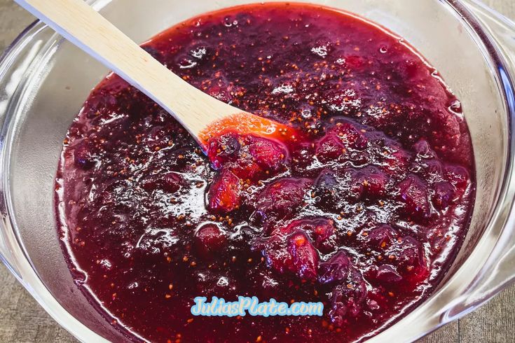 a wooden spoon in a glass bowl filled with red liquid and cranberry sauce