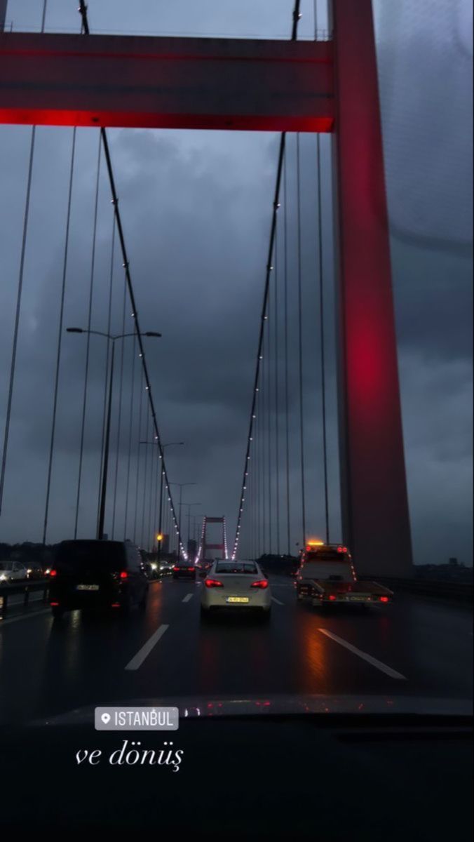 cars driving across a bridge at night with the lights turned on and dark clouds in the background