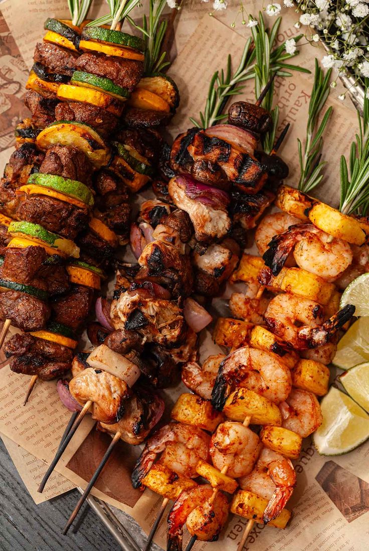 several skewered meats and vegetables are on a tray with lemon wedges