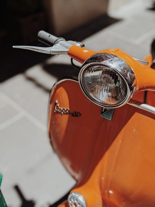 an orange scooter parked on the side of the road with its headlight up