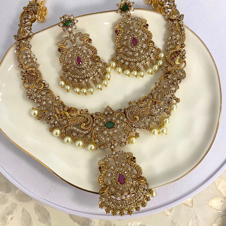 Add a touch of elegance to your collection with this beautiful gold-plated necklace set. Designed with care, it features a stunning mix of American diamonds, ruby, and emerald stones, all brought together with delicate pearls. This set isn't just jewelry; it's a statement piece perfect for weddings, festive events, or any occasion where you want to shine. The intricate design captures the essence of traditional South Asian craftsmanship while offering a modern twist. Whether you're dressing up o Elegant Gold Emerald Necklace With Intricate Design, Anniversary Gold Cubic Zirconia Kundan Necklace, Gold Cubic Zirconia Necklace For Festive Occasions, Gold Kundan Necklace With Elegant Cubic Zirconia Design, Gold Stone Work Anniversary Jewelry Sets, Gold Kundan Necklace With Cubic Zirconia Stone Work, Gold Jewelry Sets With Stone Work For Anniversary, Gold Cubic Zirconia Kundan Necklace With Elegant Design, Gold Plated Jeweled Jewelry Sets