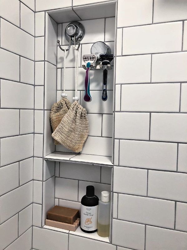 a white tiled bathroom with shelves and hooks on the wall, including a hairdryer