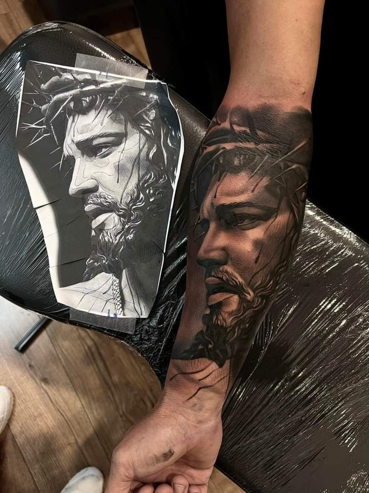 a man with a tattoo on his arm holding onto a piece of paper that has the face of jesus