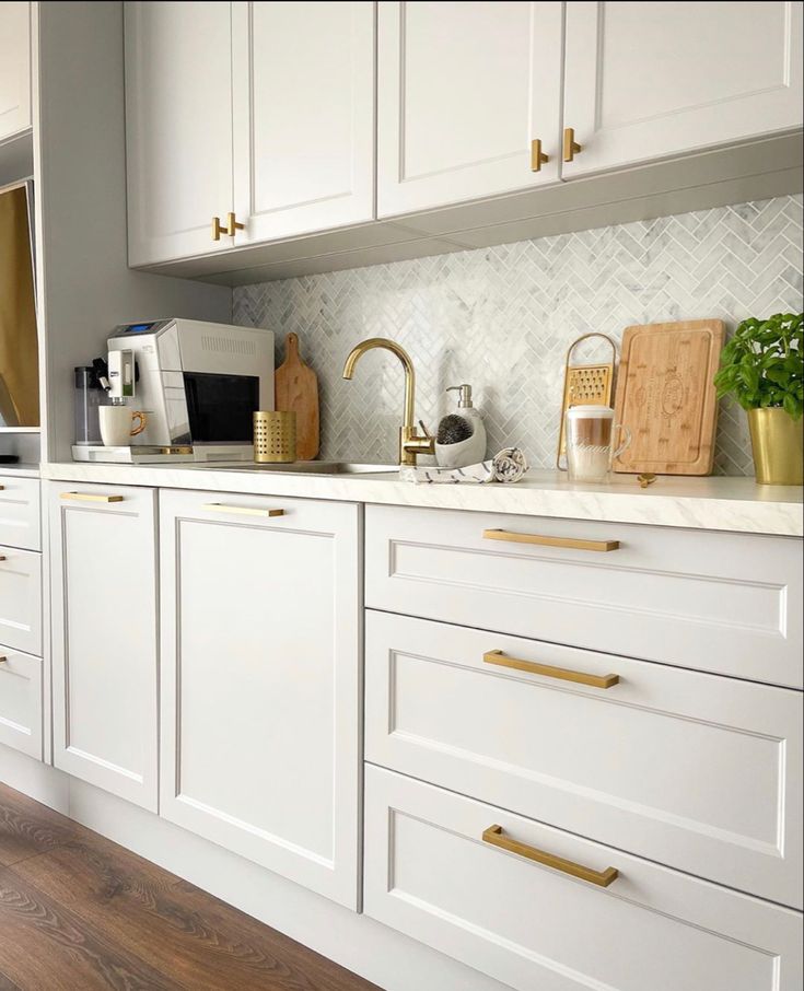 a kitchen with white cabinets and gold handles