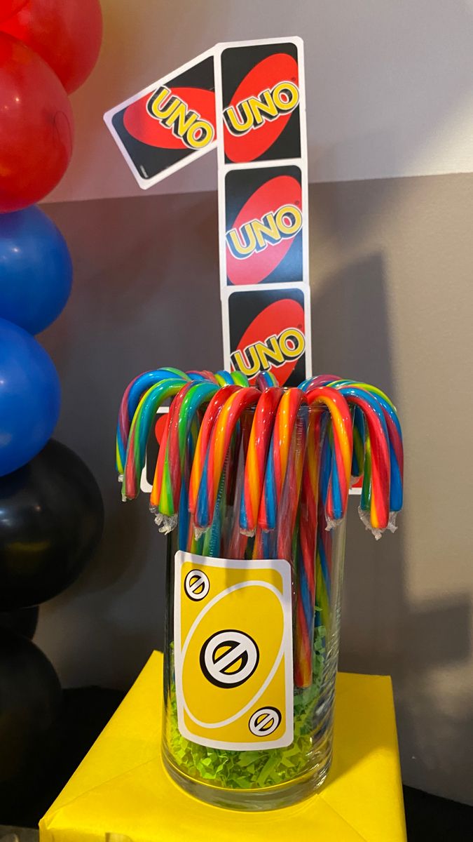 a jar filled with lollipops sitting on top of a table next to balloons