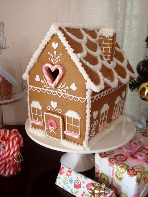 a gingerbread house is decorated with pink and white icing on a cake stand