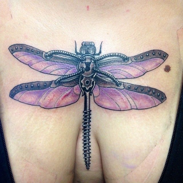 a woman's breast with a dragonfly tattoo on her chest and an ornate key attached to it