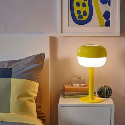 a yellow lamp sitting on top of a table next to a white nightstand with books