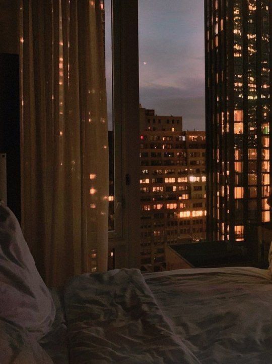 a bedroom with a view of the city at night from it's window sill