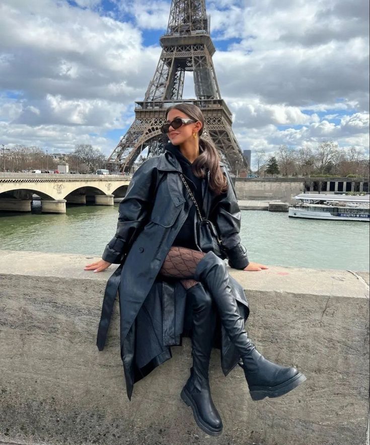 a woman sitting on the wall in front of the eiffel tower