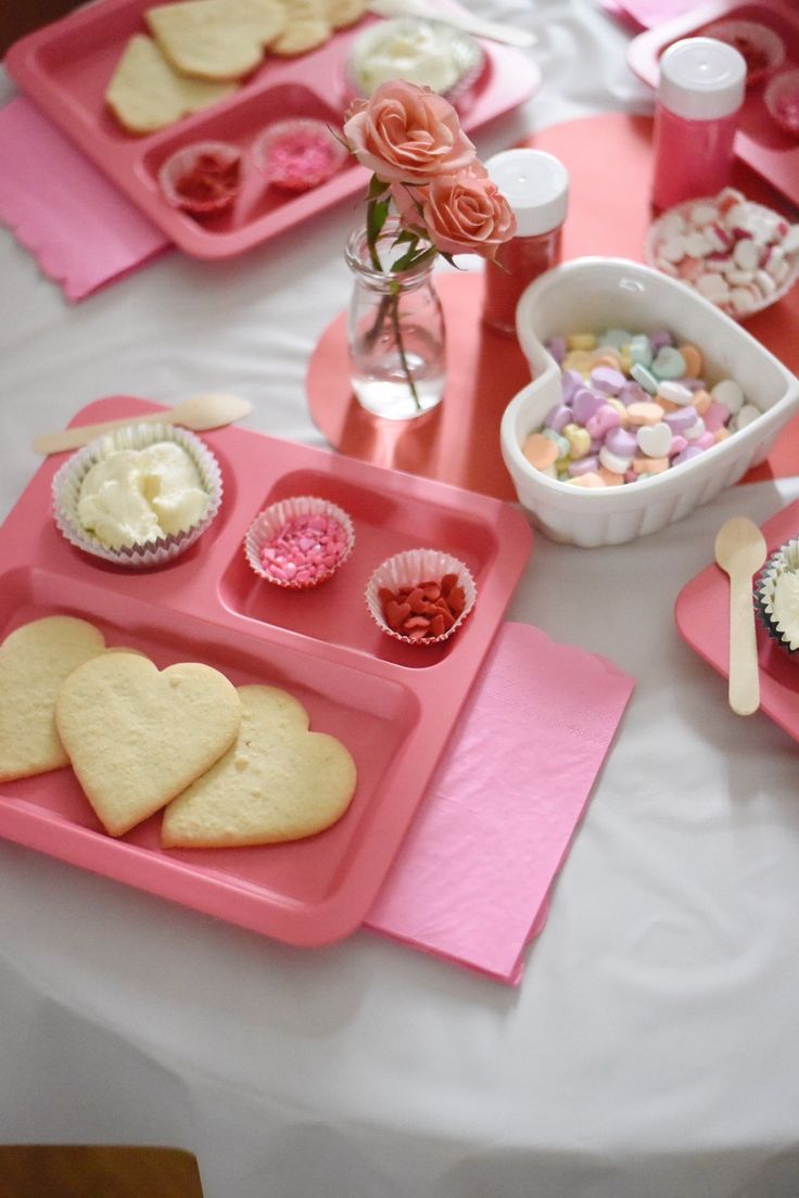 a table topped with pink trays filled with cupcakes and heart shaped cookies