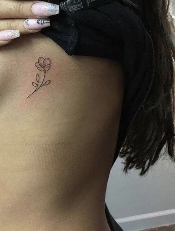 a woman's stomach with a small flower tattoo on her left side ribcage