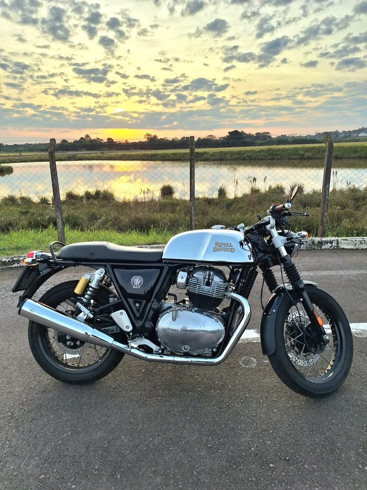 a motorcycle parked in a parking lot next to a body of water with the sun setting behind it