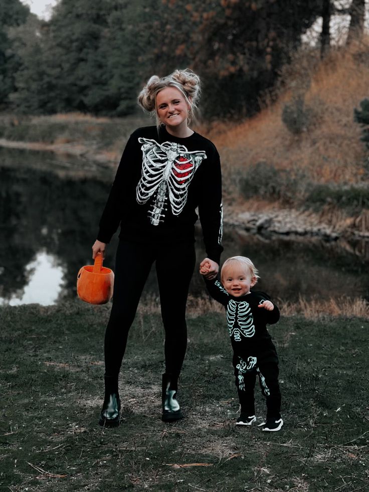 a woman and child dressed up in halloween costumes holding hands while standing next to a body of water