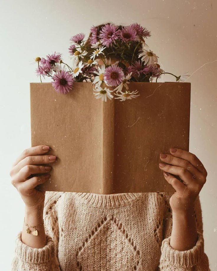 a woman holding up a brown box with flowers in it's head and covering her face