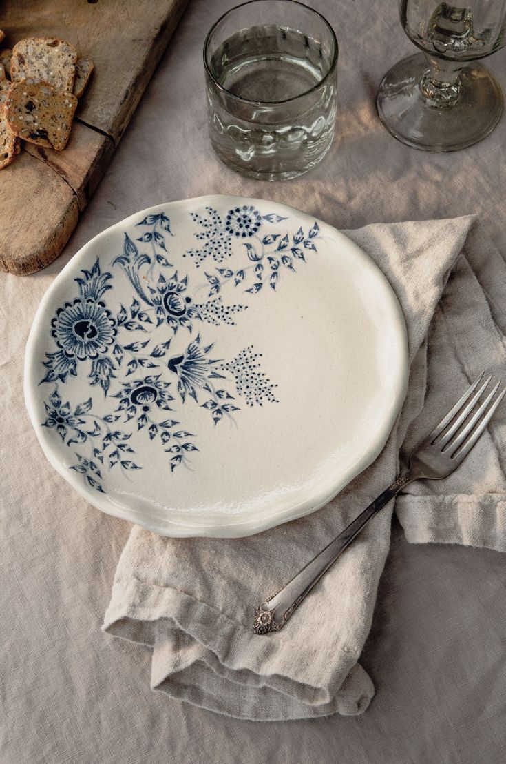 a white plate with blue flowers on it next to two glasses and a cutting board