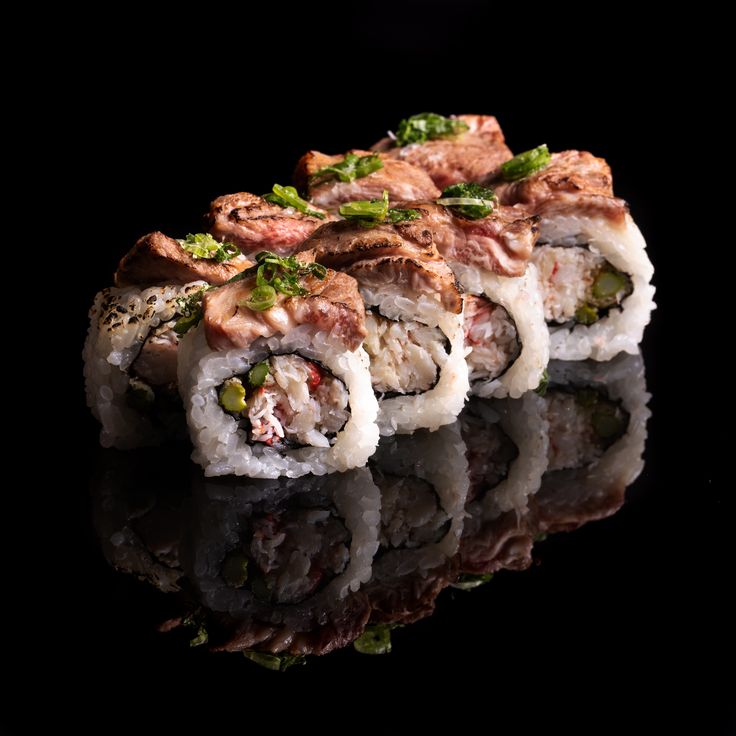 three pieces of sushi on a black surface with reflections in the water and dark background