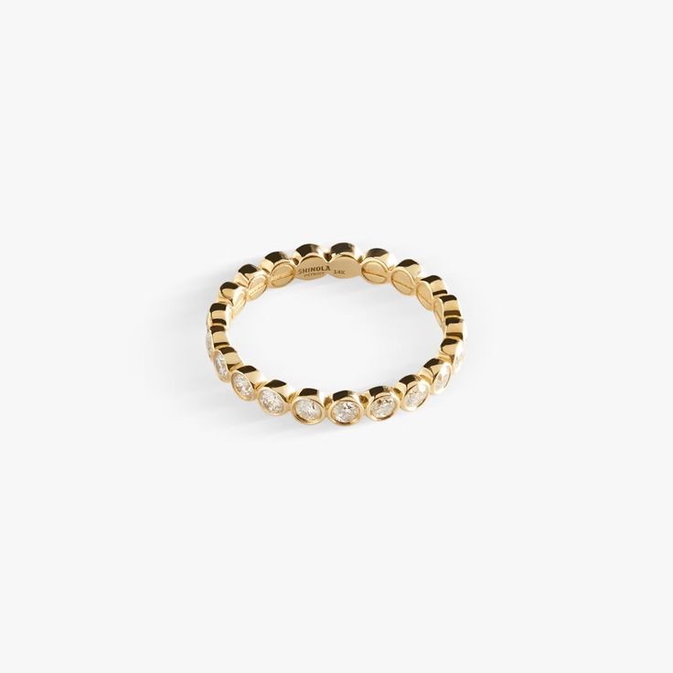 the gold beaded ring is set with three small white stones and sits on a plain surface