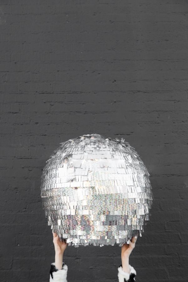 a person holding up a disco ball in front of a black wall with white fur on it