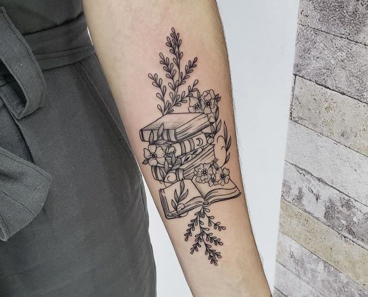 a tattoo on the arm of a person with a book and flowers in front of it