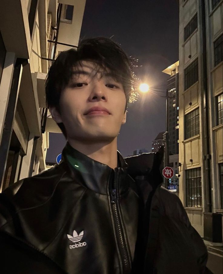 a young man standing in front of a tall building at night with his eyes closed