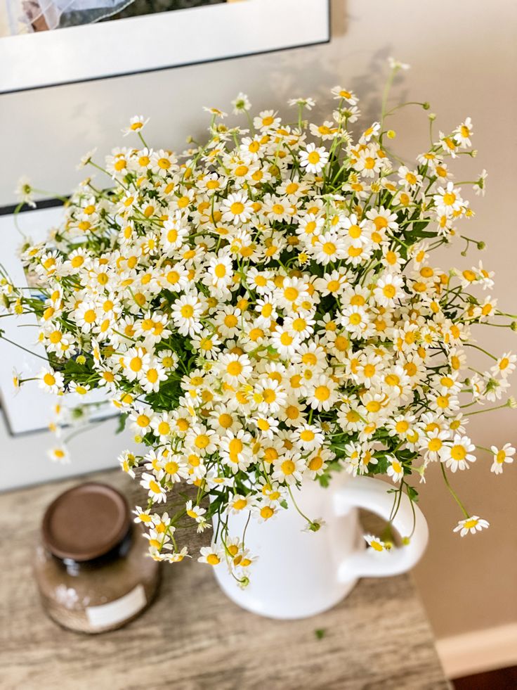 a bouquet of daisies in a white coffee cup on a table next to a framed photograph