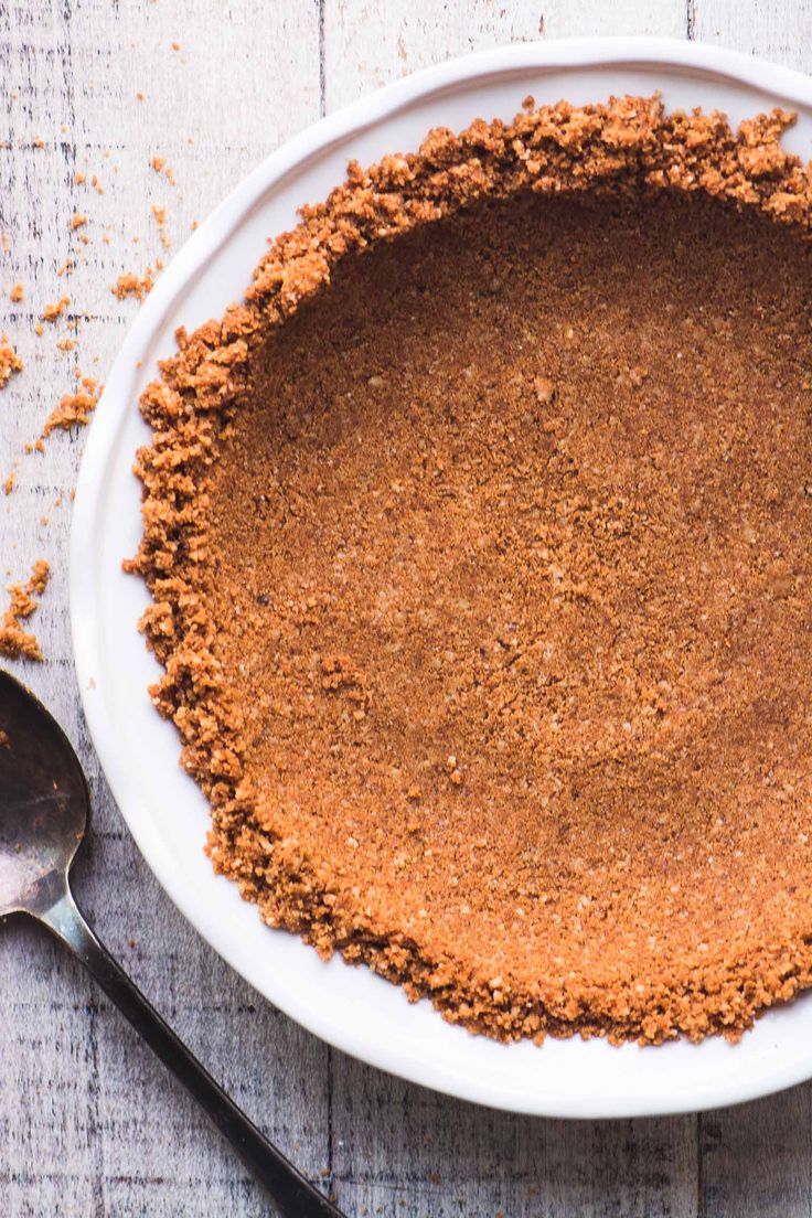 a pie crust on a white plate with a spoon next to it and a piece of bread crumbs in the middle