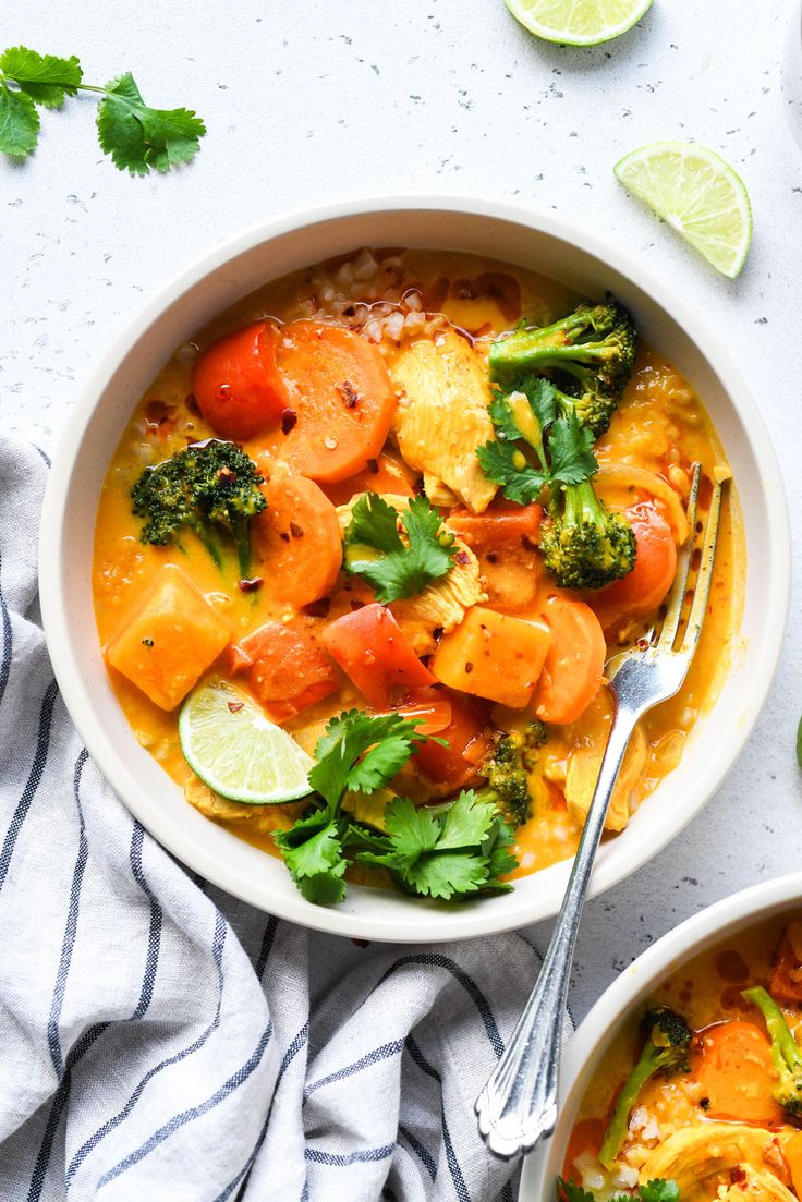 two bowls filled with chicken and veggies on top of a white table next to limes