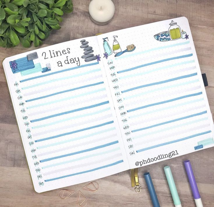 an open planner sitting on top of a wooden table next to some pens and candles