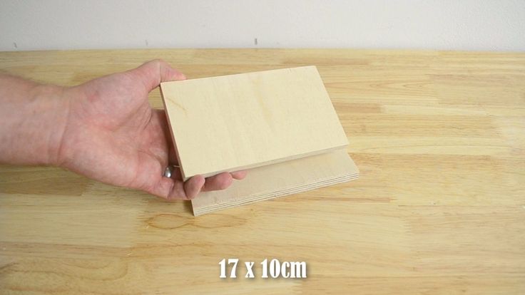 a hand holding a piece of wood on top of a wooden table