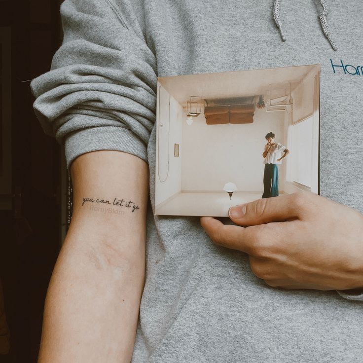 a person with a small tattoo on their arm holding an open photo album in front of them