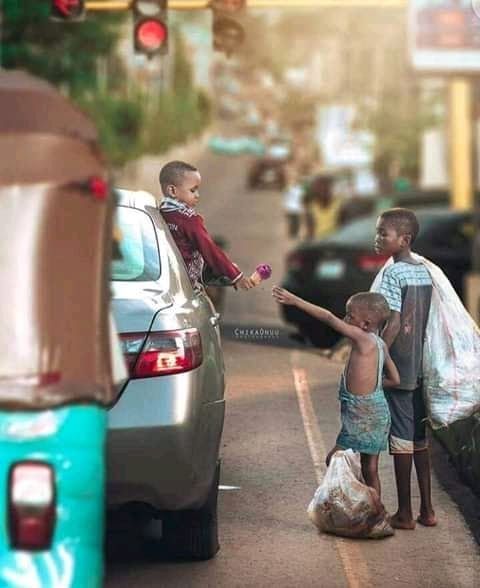 two young boys standing on the side of a road next to a car and another boy holding something in his hand