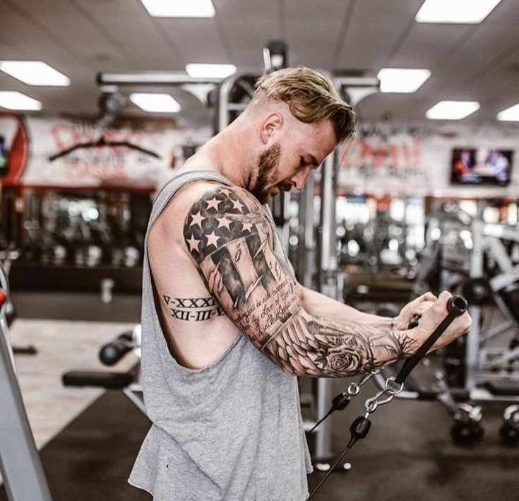 a man with tattoos on his arm working out in the gym while looking at his cell phone