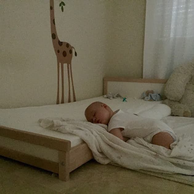 a baby laying on top of a bed next to a stuffed giraffe wall decal