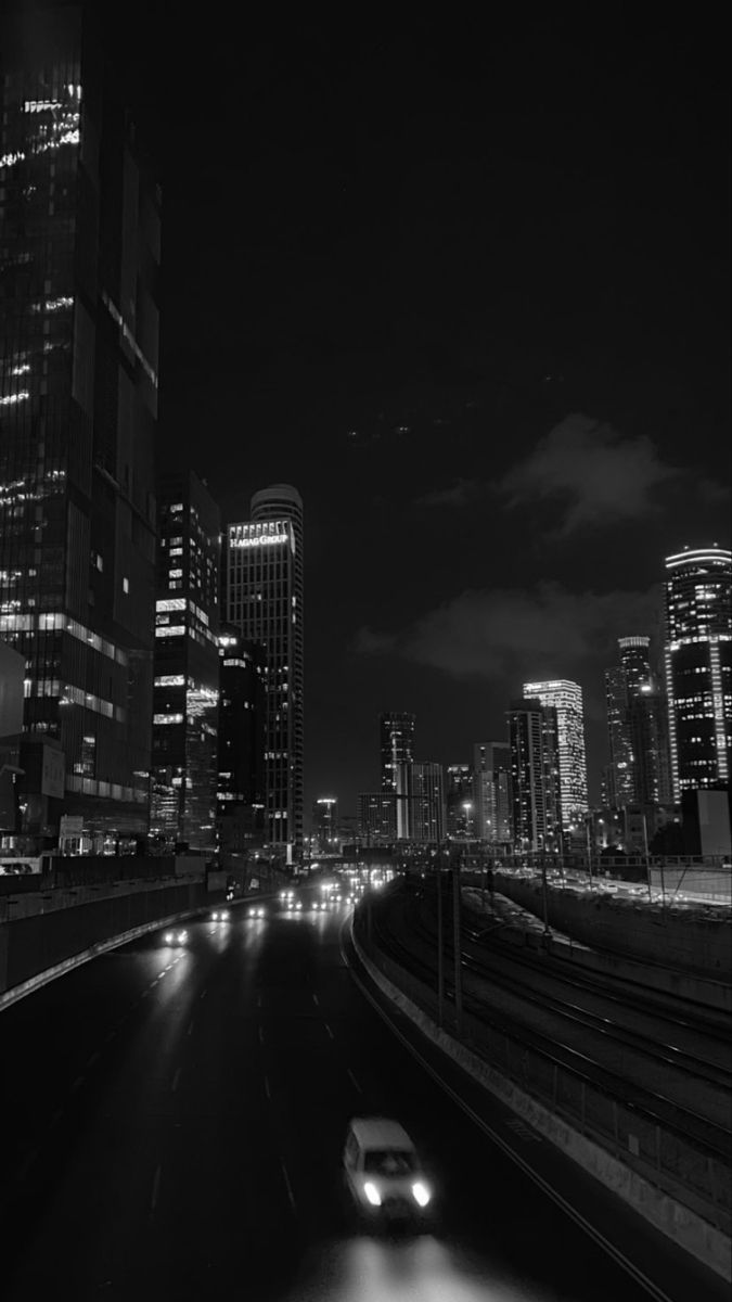 a black and white photo of a city at night with cars driving down the road