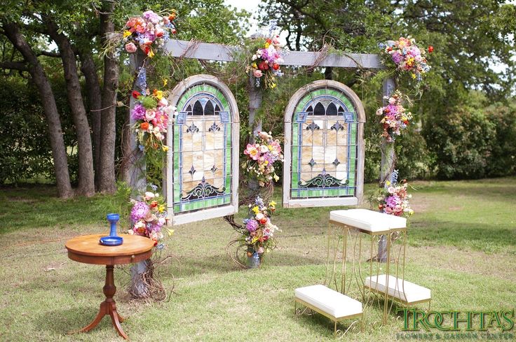 an outdoor ceremony setup with stained glass windows and flowers on the arbors, in front of trees