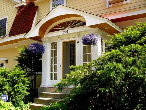 a yellow house with white trim and blue flowers on the front door is surrounded by greenery