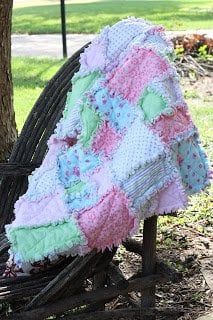 a baby quilt sitting on top of a wooden bench next to a tree in a park