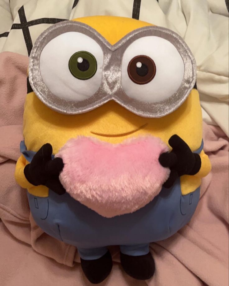 a stuffed toy with eye glasses on it's face and heart shaped pillow in the shape of a minion