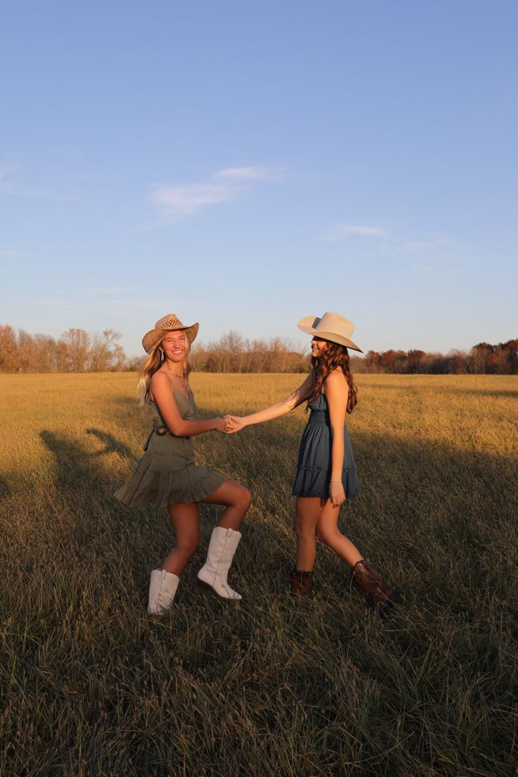 two women in hats are sitting on the grass and holding hands with each other,