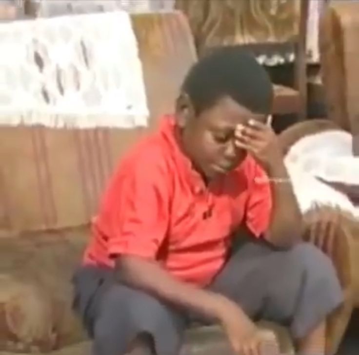 a young boy sitting on top of a couch holding his hand up to his face