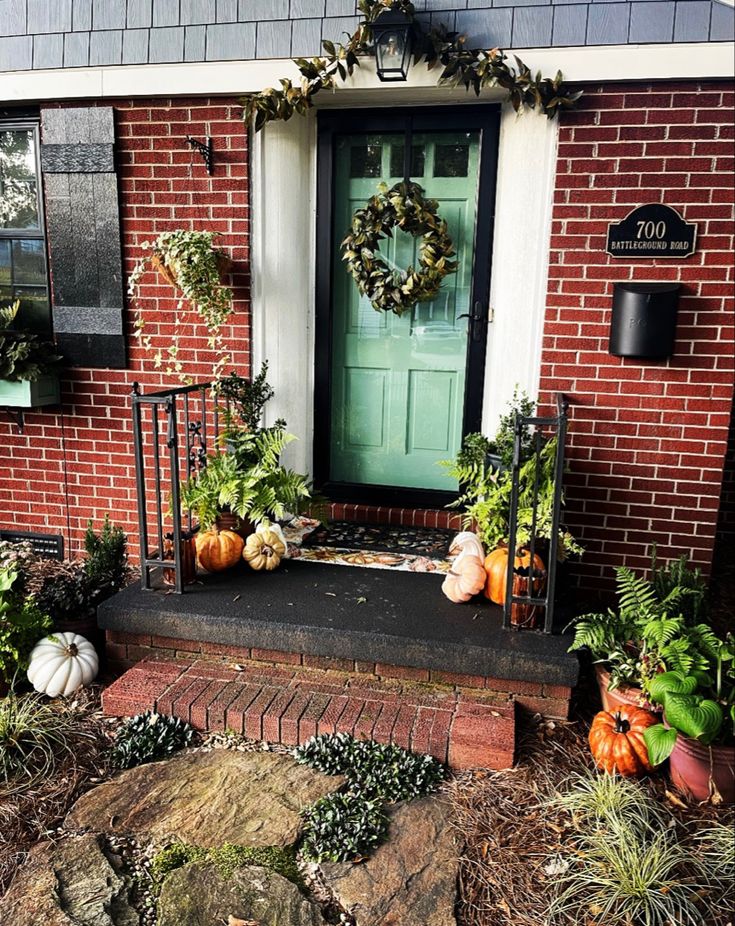 a front porch decorated for fall with pumpkins and greenery on the steps next to the door