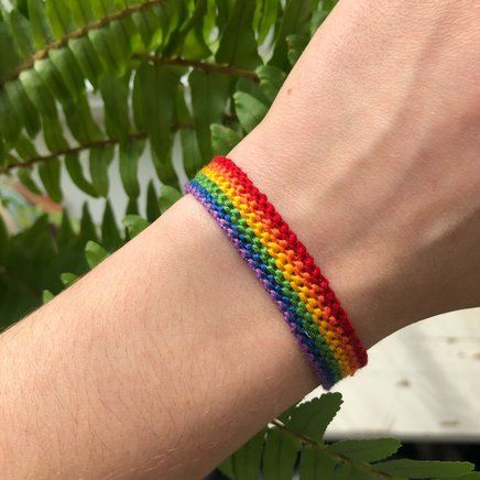 a person wearing a rainbow colored bracelet on their arm with leaves in the back ground