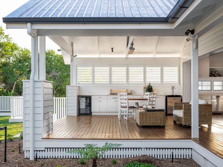 an outdoor kitchen and dining area on the back deck of a white house with wood flooring