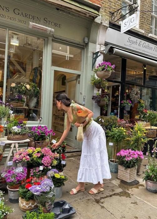 a woman tending to potted plants in front of a flower shop