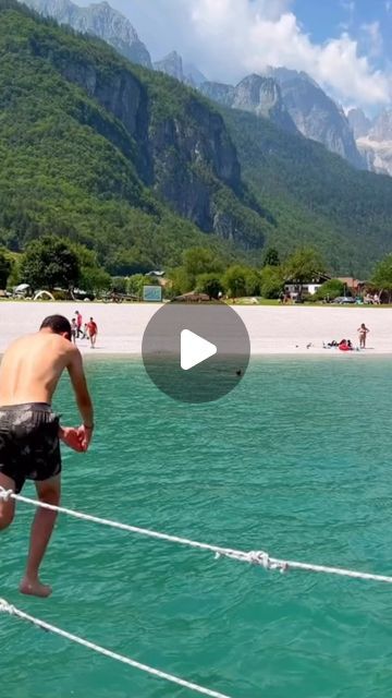 a man is standing on a rope in the water with mountains in the back ground